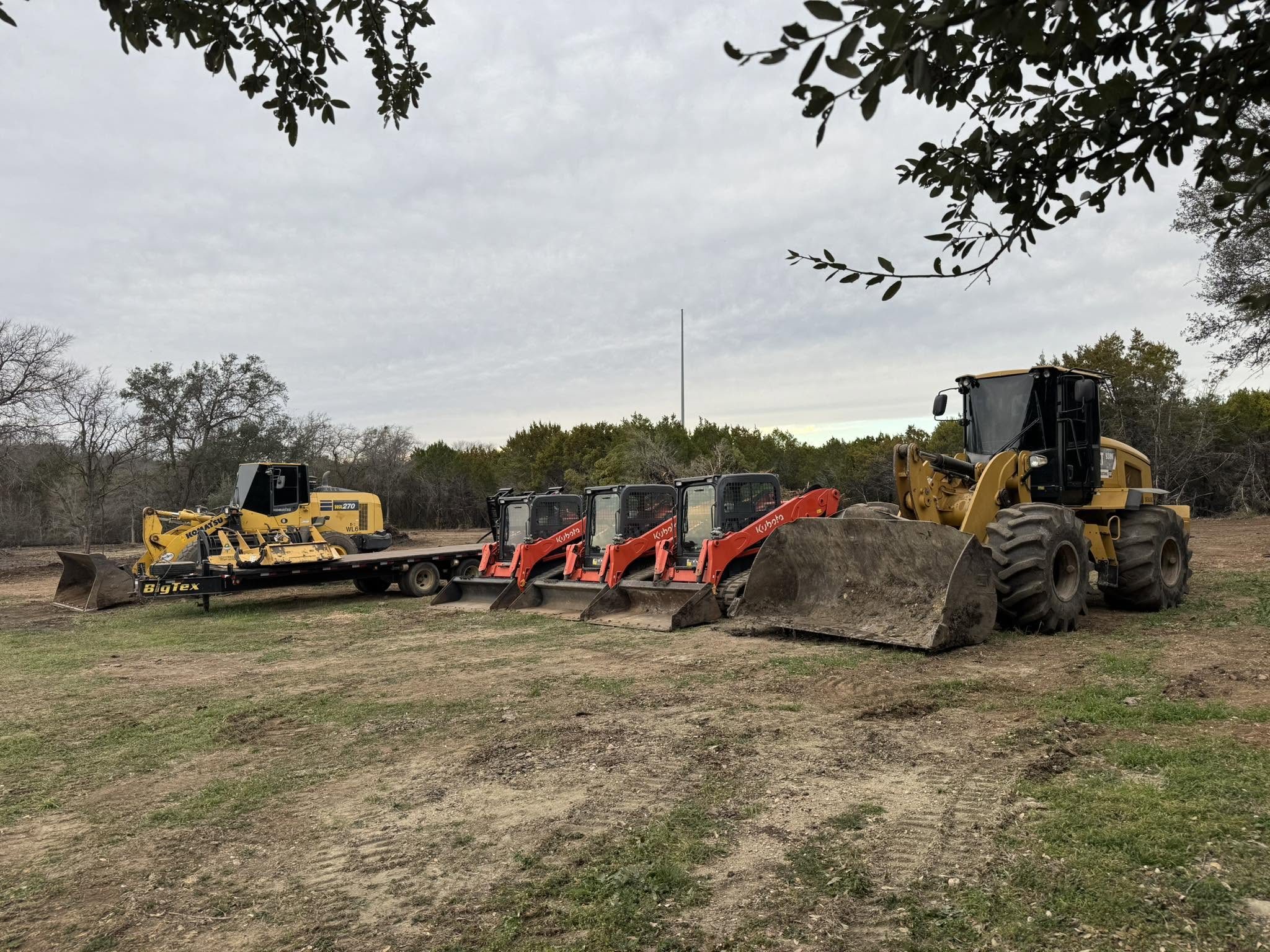 A wheel loader, three skid steers and a Komatsu on a trailer lined up on the Earth Movers lot